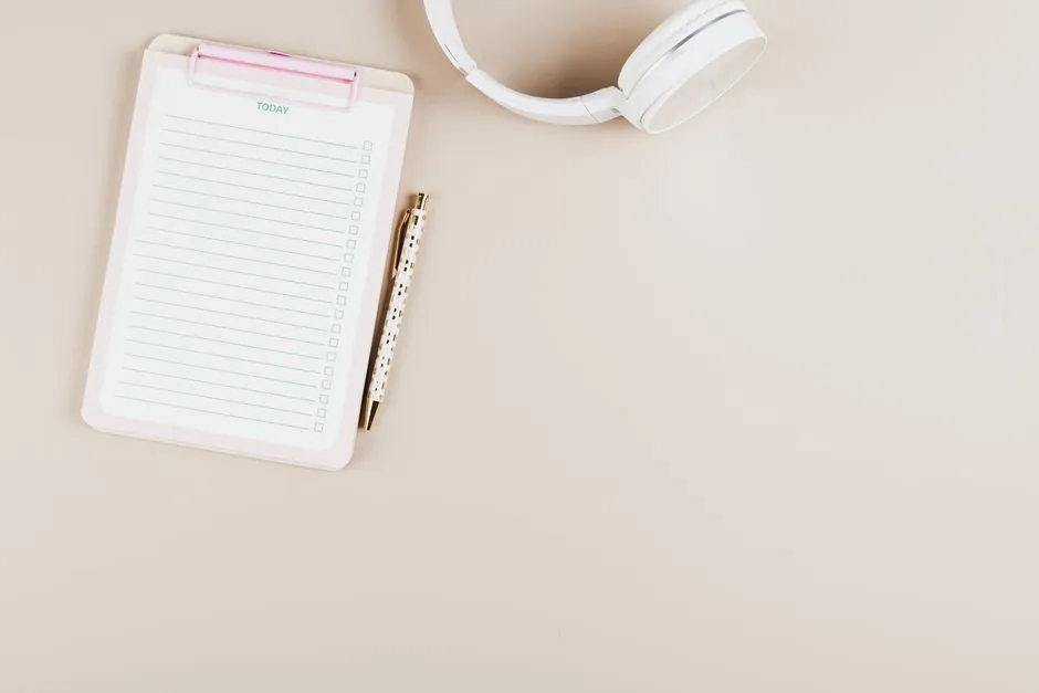 Un agencement simpliste d'un bloc-notes, d'un stylo et d'écouteurs sur un fond blanc.