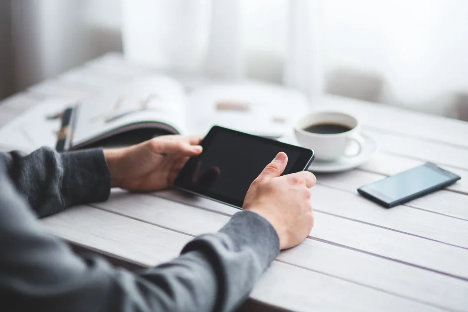 Personne lisant la lettre hebdomadaire sur une tablette à son bureau, un café à côté.