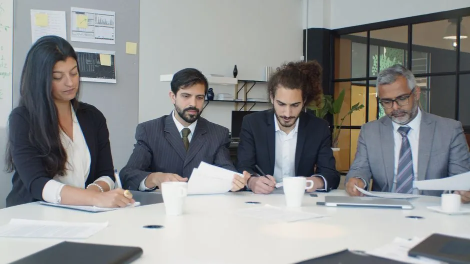 Groupe de professionnels engagés dans une réunion d'équipe autour d'un bureau dans un cadre de bureau moderne.